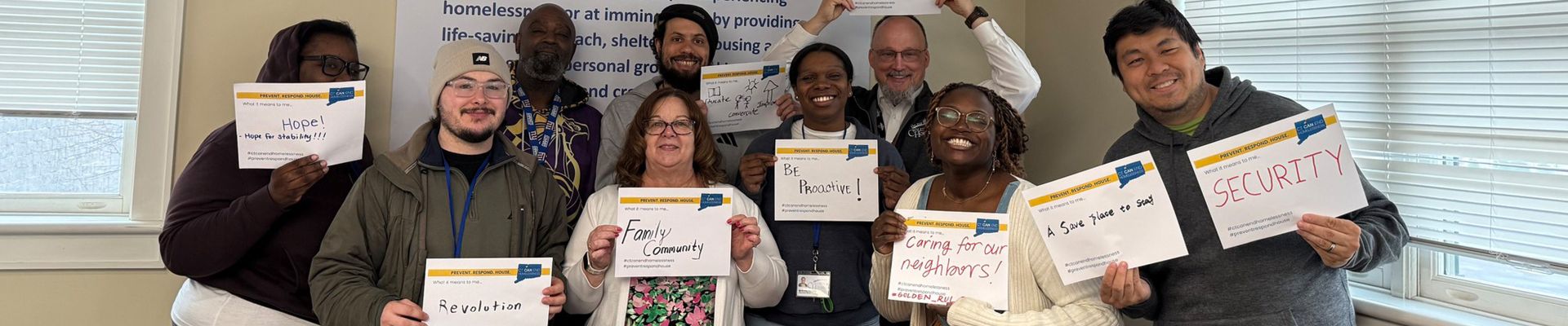 Group of people holding up signs with different words for what CT Can End Homelessness means to them. The words written are "Hope! Hope for stability," "Revolution," "Family and community," "Educate, conversate and improve," "Be proactive," "Caring for our neighbors," "A safe place to stay," and "security"