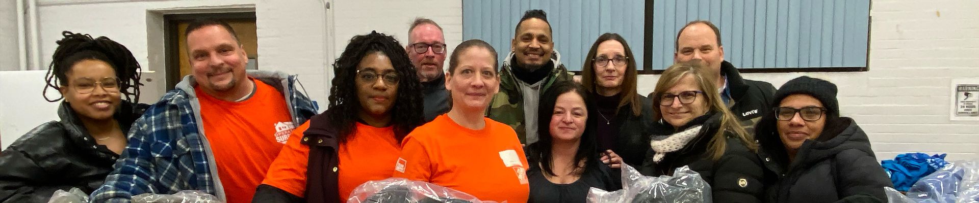 Group of people posing together. Some people are wearing orange t shirts and other are wearing winter jackets