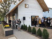Group of people gathered in front of building. A woman is standing at a microphone giving a speech