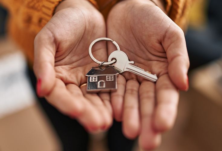 Pair of cupped hands holding out a key with a house-shaped keychain attached to it
