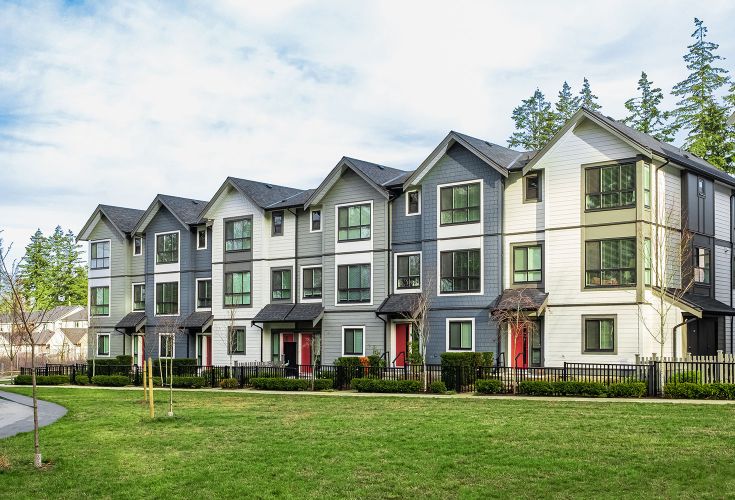 A row of gray, white, and blue condos with bright red doors and fenced off front yards