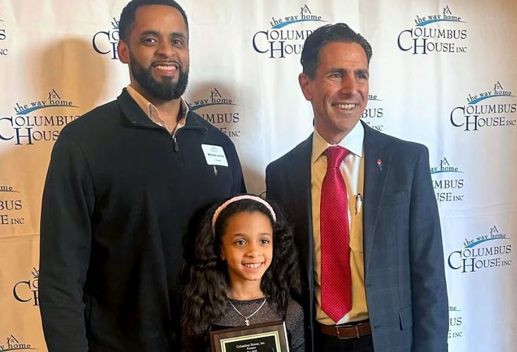 Two men posing with a young girl who is holding her award