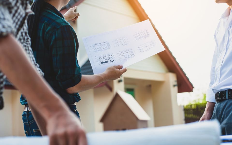 Man pointing to a house while holding a floor plan blueprint